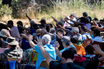 an outdoor prayer service, people with hands raised 