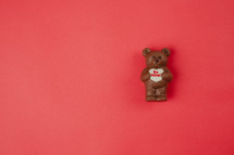 A chocolate bear holding a Valentine heart on a red background.