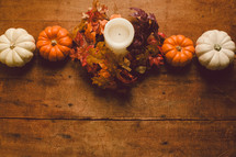 Miniature pumpkins and a candle with a wreath of fall leaves on a wooden table -- Thanksgiving decor.