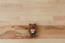 A chocolate bear holding a Valentine heart on a wooden background.
