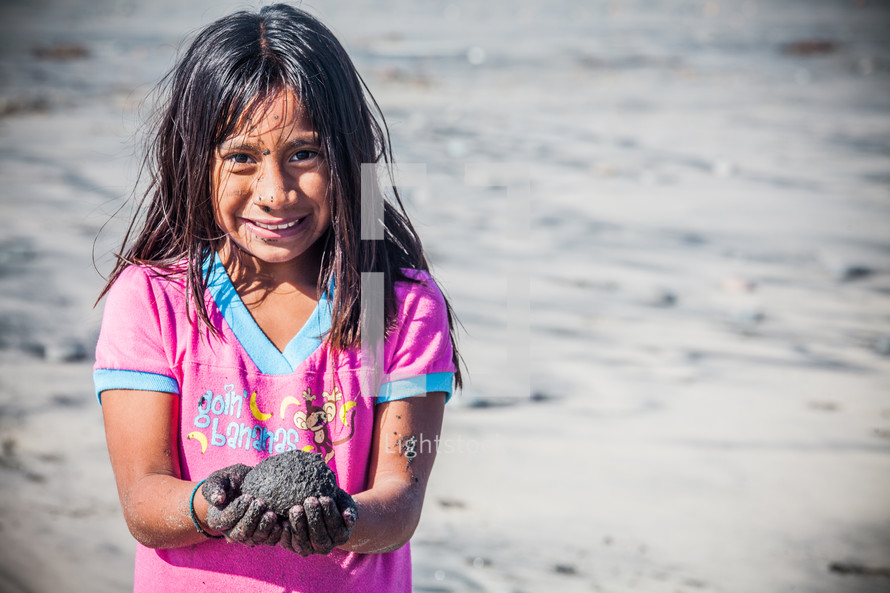 girl child holding a rock on a beach 