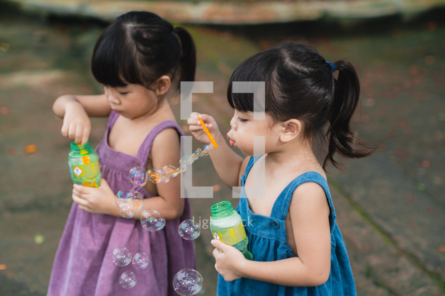 toddler girls blowing bubbles outdoors 