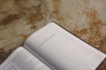 Bible open to the New Testament on a concrete floor.