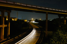 A night scene of a highway under an overpass lit by headlights.