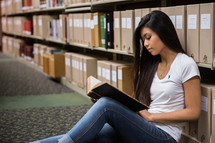 woman sitting on a floor of a library reading 