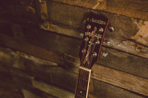 Guitar neck leaning against a wooden wall.