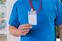 Man in a blank blue tshirt holding up a lanyard.