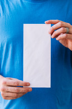 Close up of a man holding up a blank flyer against his torso.