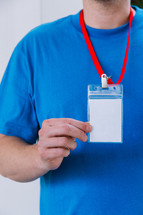 Close up of a man in a blank blue tshirt holding up a lanyard.