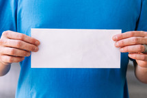 Close up of a man holding up a blank flyer against his torso.