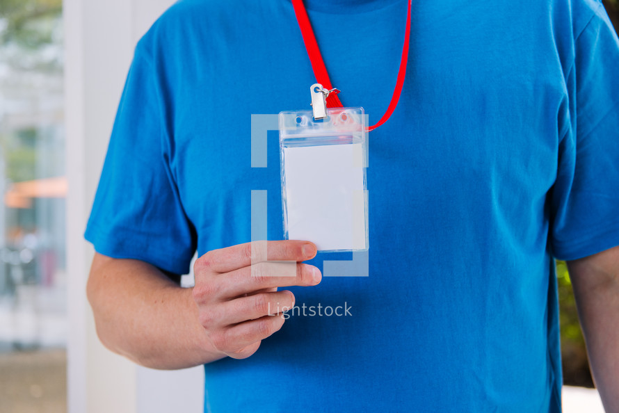 Man in a blank blue tshirt holding up a lanyard.