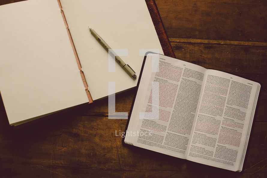 Empty journal with blank pages and a pen on a wooden table with an open Bible.