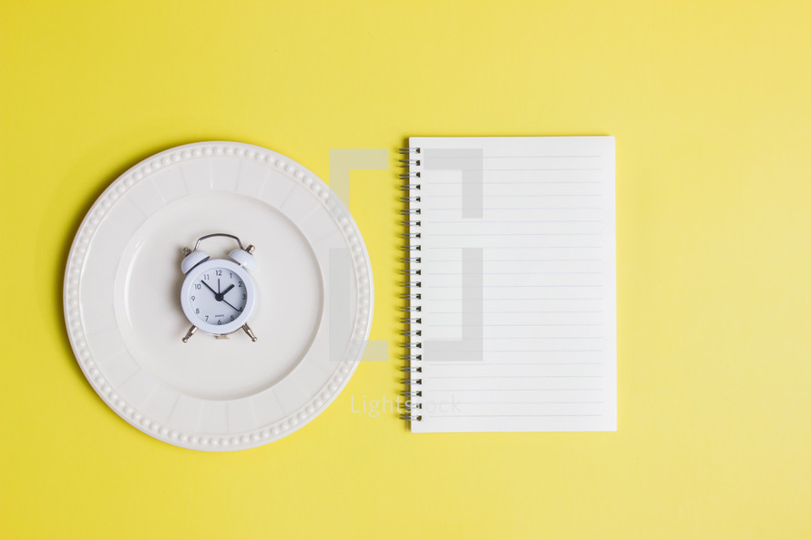 Diet concept with notebook and clock over the yellow background. 