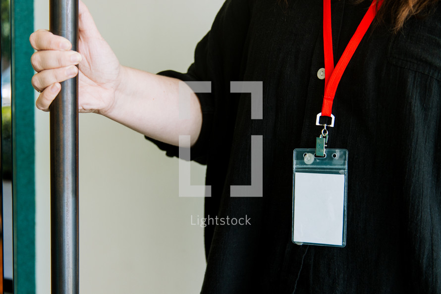 Woman in a black shirt wearing a lanyard while holding a door open.