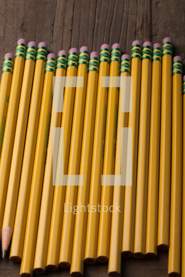 Wooden pencils laying side-by-side on a wooden surface.