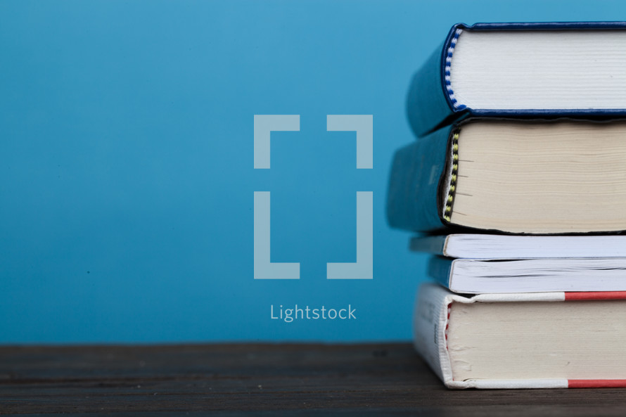 Stack of books on a wooden surface against a blue background.