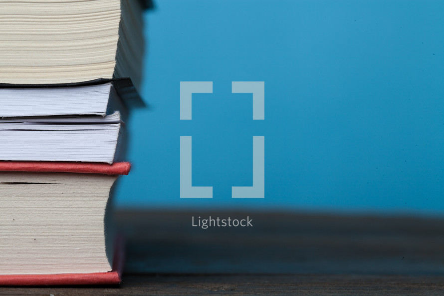 Stack of books on a wooden surface against a blue background.