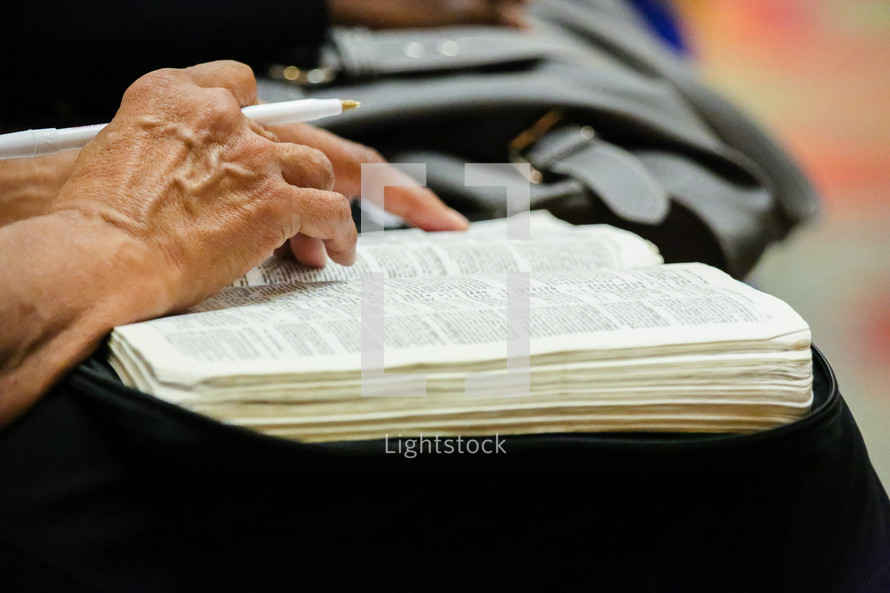 A elderly woman's hand holding a pen at a Bible study 