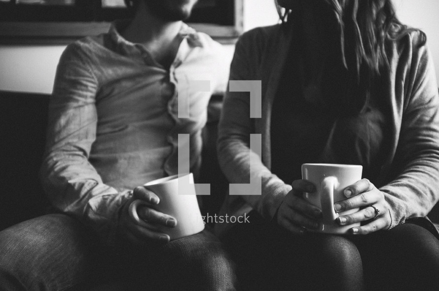 A young couple sitting on a couch drinking coffee