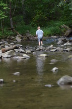 a boy standing in shallow water of a river 