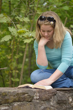 woman reading the bible while sitting outside on a wall. 
