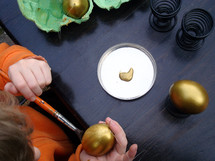 A child painting an egg with gold paint.