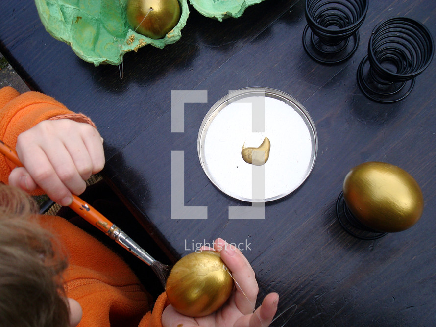 A child painting an egg with gold paint.
