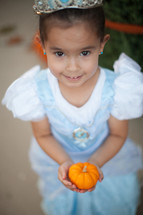 a little girl in a princess costume holding a pumpkin 