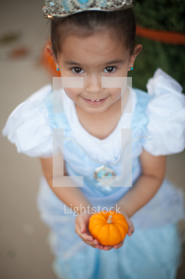 a little girl in a princess costume holding a pumpkin 
