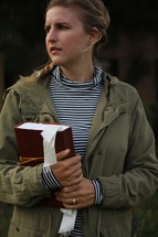 a young woman in a coat holding a Bible 