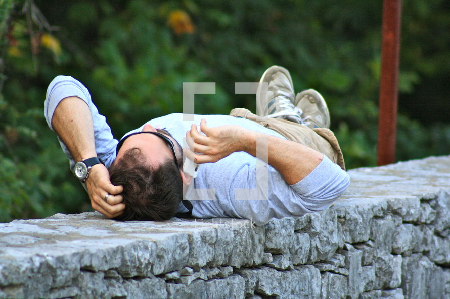 Man lying on back, outdoors, on cell phone