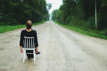 a woman sitting in a chair in the middle of a dirt road 