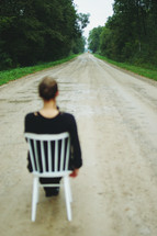 a woman sitting in a chair in the middle of a dirt road 