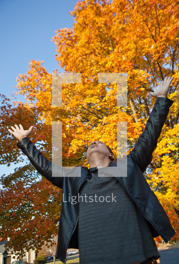 man with his hands raised in worship to God under fall leaves