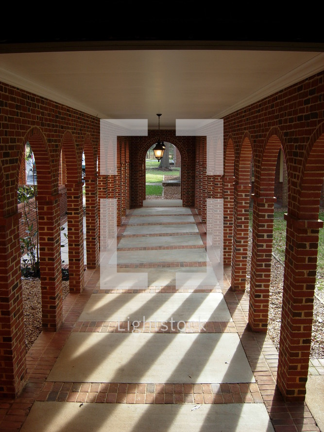 A long hall or corridor shows archways where columns of sunlight penetrate and light the path of this hallway in a church in the southeastern United States. 