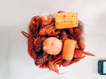 Crawfish boil in a bowl with a potato, carrot, and corn on the cob.