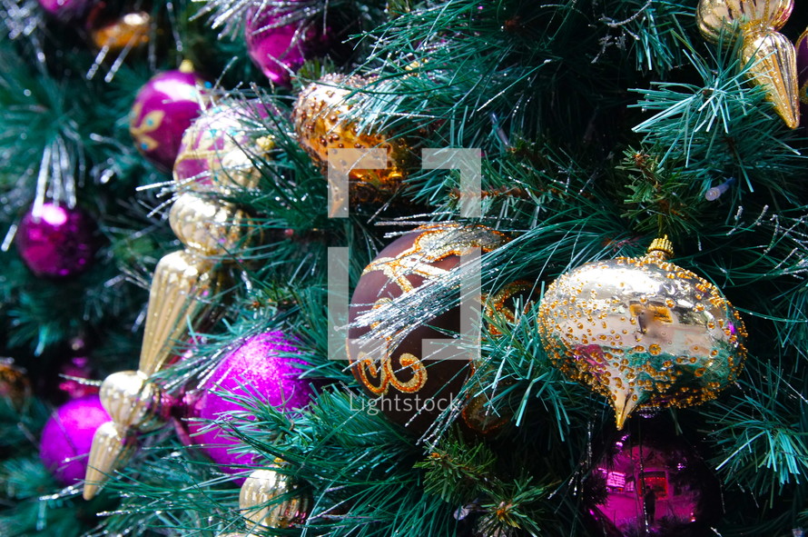 Purple and gold ball ornaments hanging from pine Christmas tree.