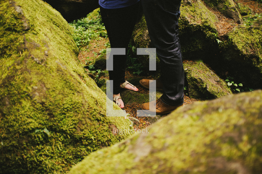 feet of a couple standing on moss covered rocks