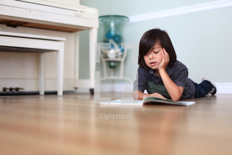 Boy reading book on bedroom floor