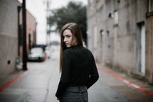 a young woman walking down a street and stopping to look back at the camera 