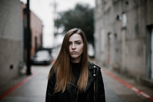 a young woman standing on a city street facing the camera with sad eyes