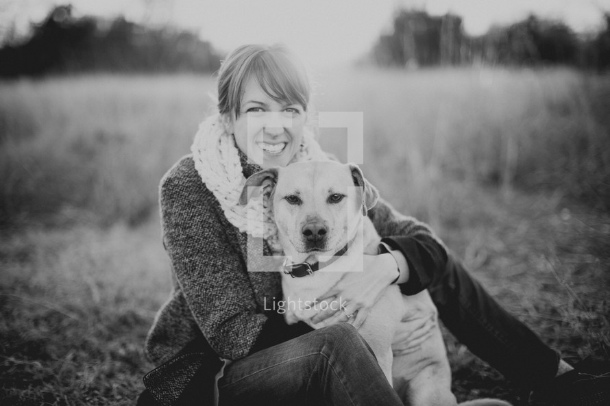 Smiling woman sitting with her dog in a field.