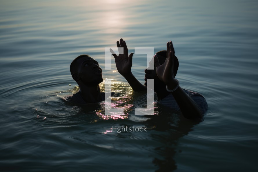 Baptism. Silhouette of two young black men in worship in the water at sunset