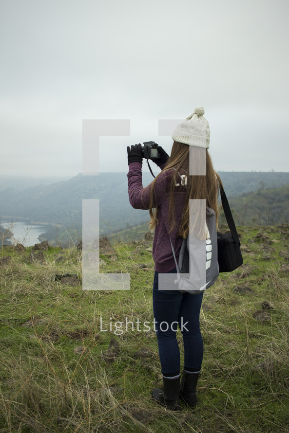 a woman taking a video standing on a mountaintop 