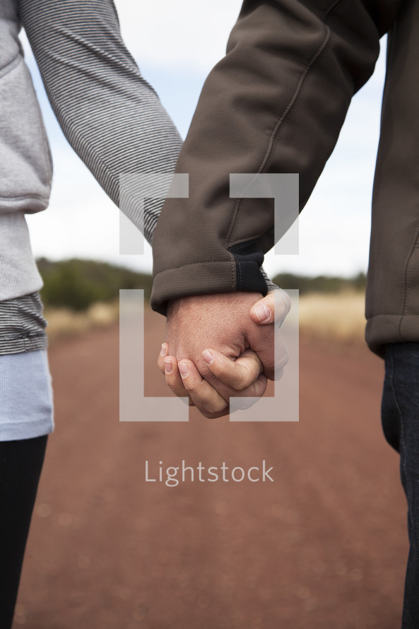 couple holding hands on a dirt road 