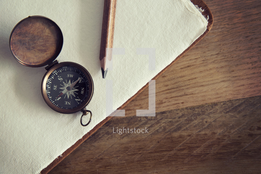A pencil and compass lying on blank sheets of white paper.
