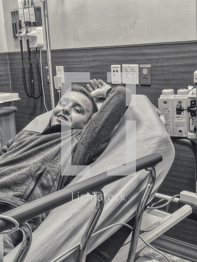 A teenage boy lying in a hospital bed with a bandaged hand waiting to get stitches 