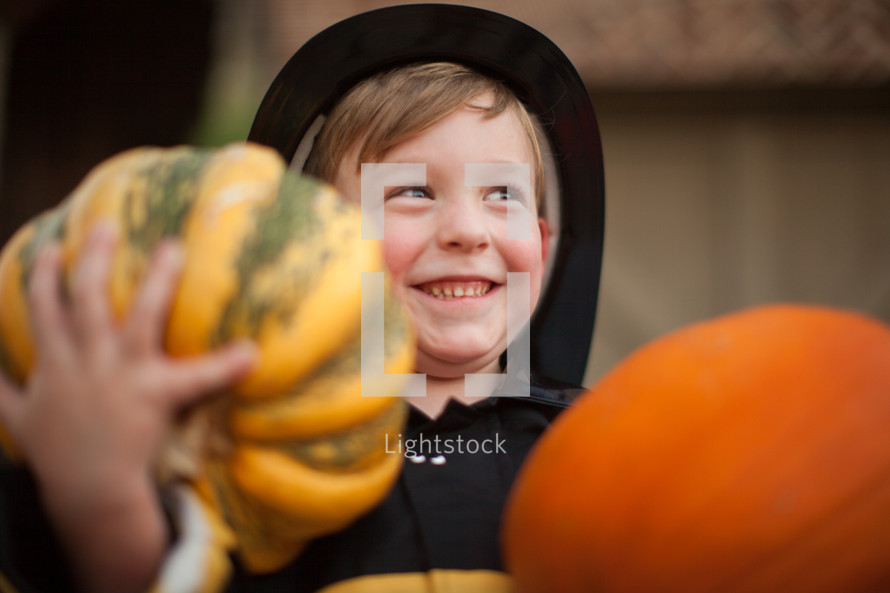 a boy child in a halloween costume holding pumpkins 
