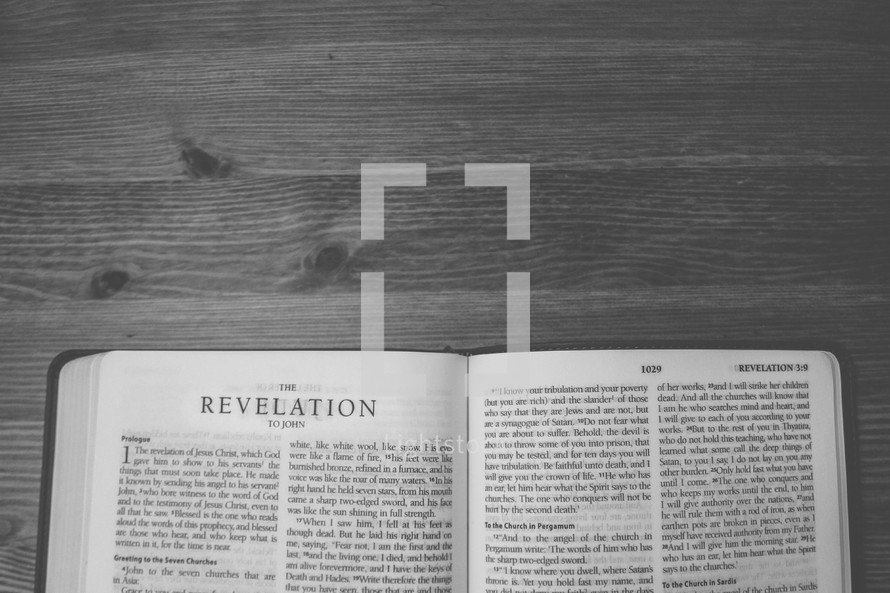 Bible on a wooden table open to the book of Revelation.