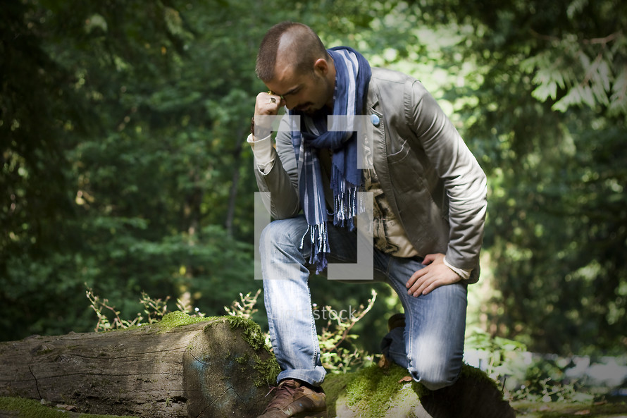 Tebowing:  man crouched or kneeling on logs with his fist to his forehead in a forest.